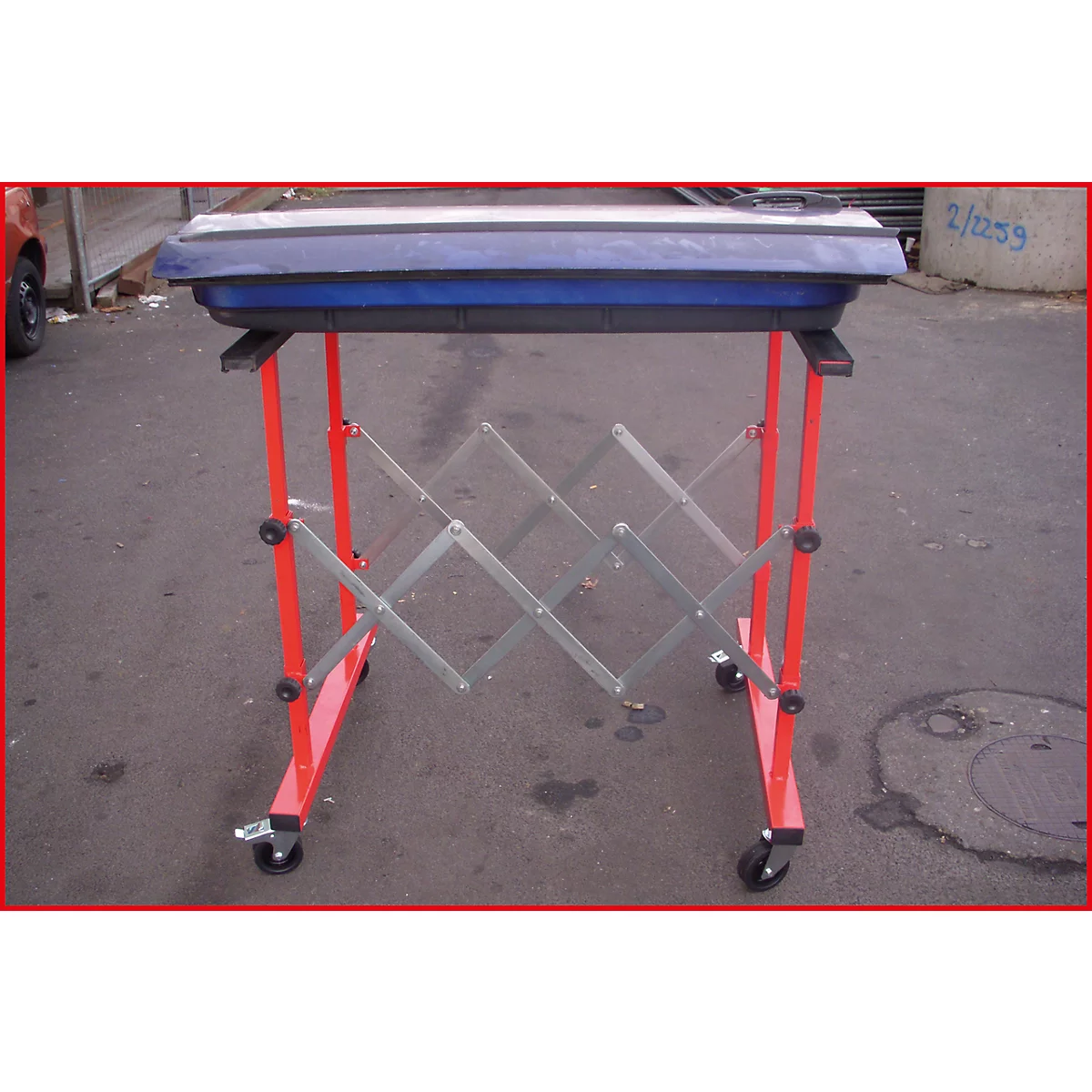 Ein roter, rollbarer Werkzeugtisch mit blauem Deckel. Das Z-förmige Gestell kann ausgezogen werden.